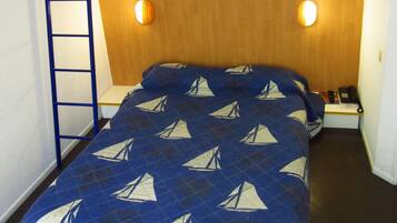 Uma cama beliche com colcha estampada com um veleiro azul, cabeceira de madeira e duas luminárias de cabeceira.