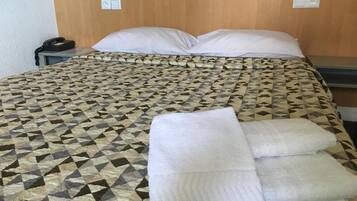 A neatly made bed with a patterned bedspread, two pillows, and a folded white towel on the bed.