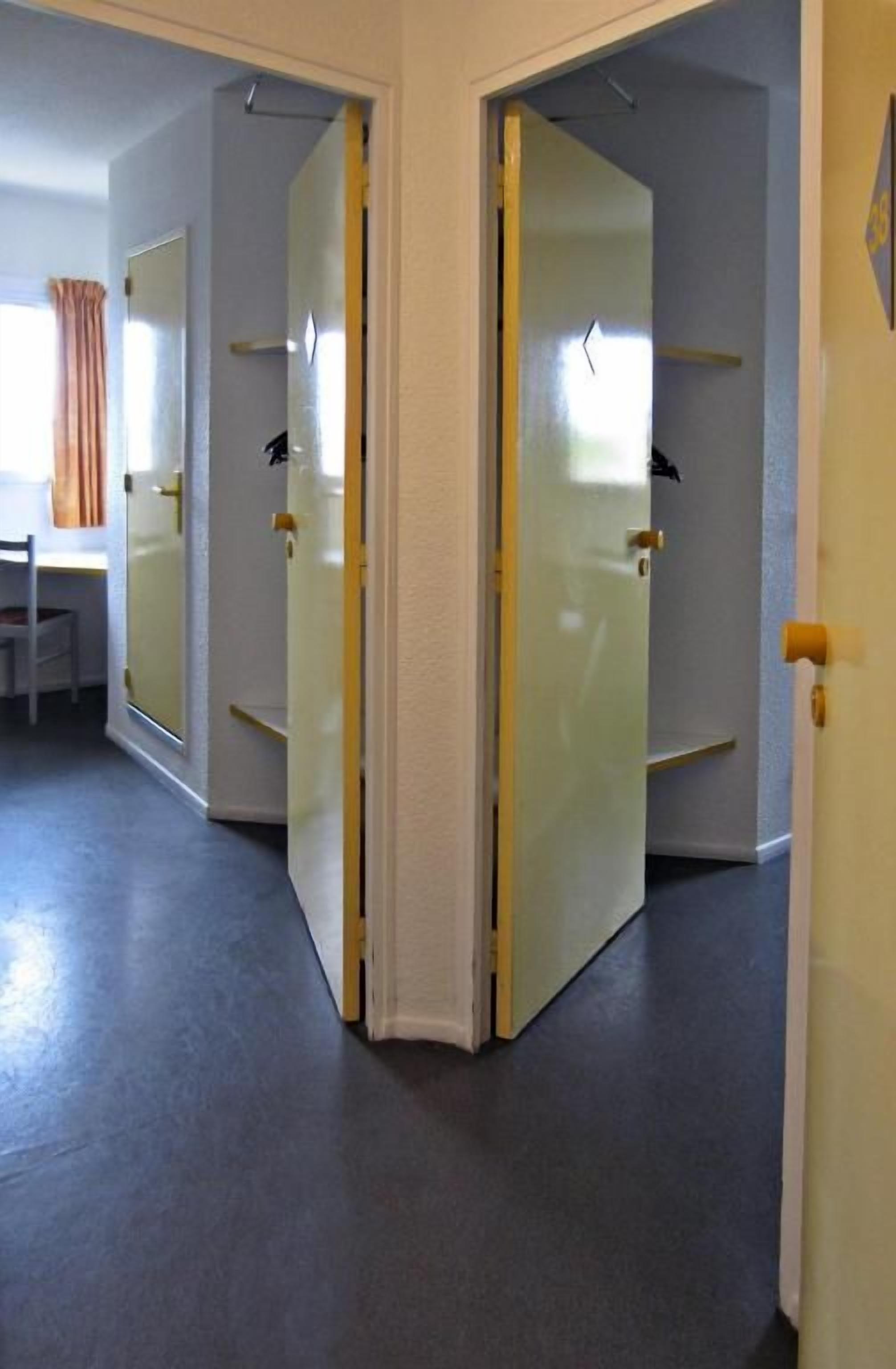 Un pasillo con una puerta cerrada, una ventana con cortina y una silla.