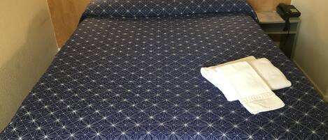 Een keurig opgemaakt bed met een bedsprei met een geometrisch patroon, twee bedlampjes en een telefoon op een nachtkastje.