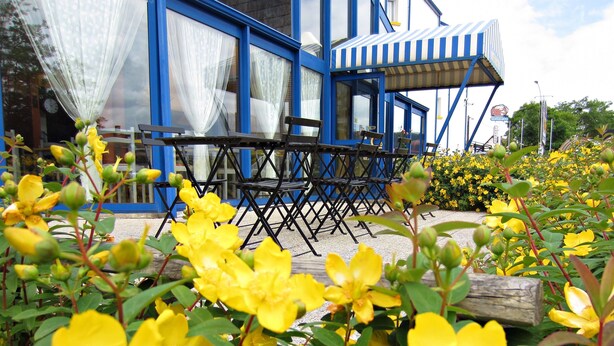 A blue building with large windows and a striped awning. There are tables and chairs outside. - Hotel Noctuel - Blois (Saint-Gervais-la-Foret)