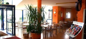 A restaurant with indoor seating, a potted plant, and a menu display.