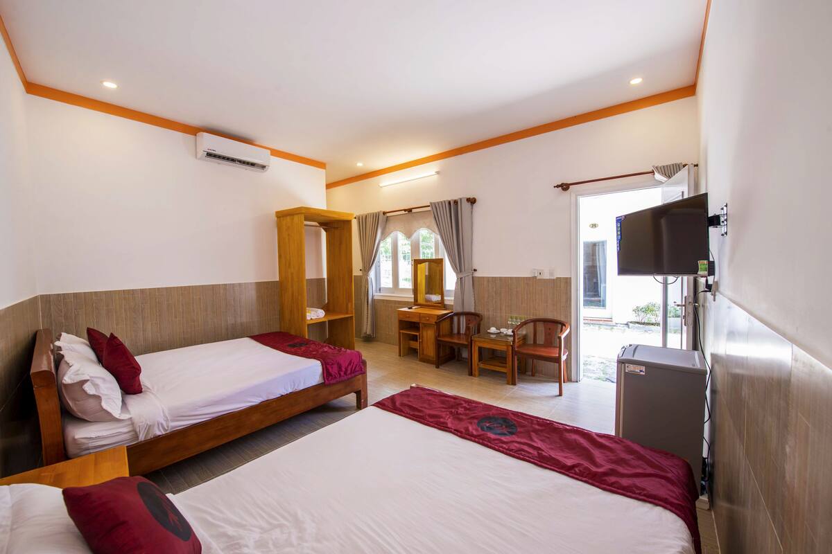 A hotel room with two single beds, a desk, a chair, a TV, and a small refrigerator.