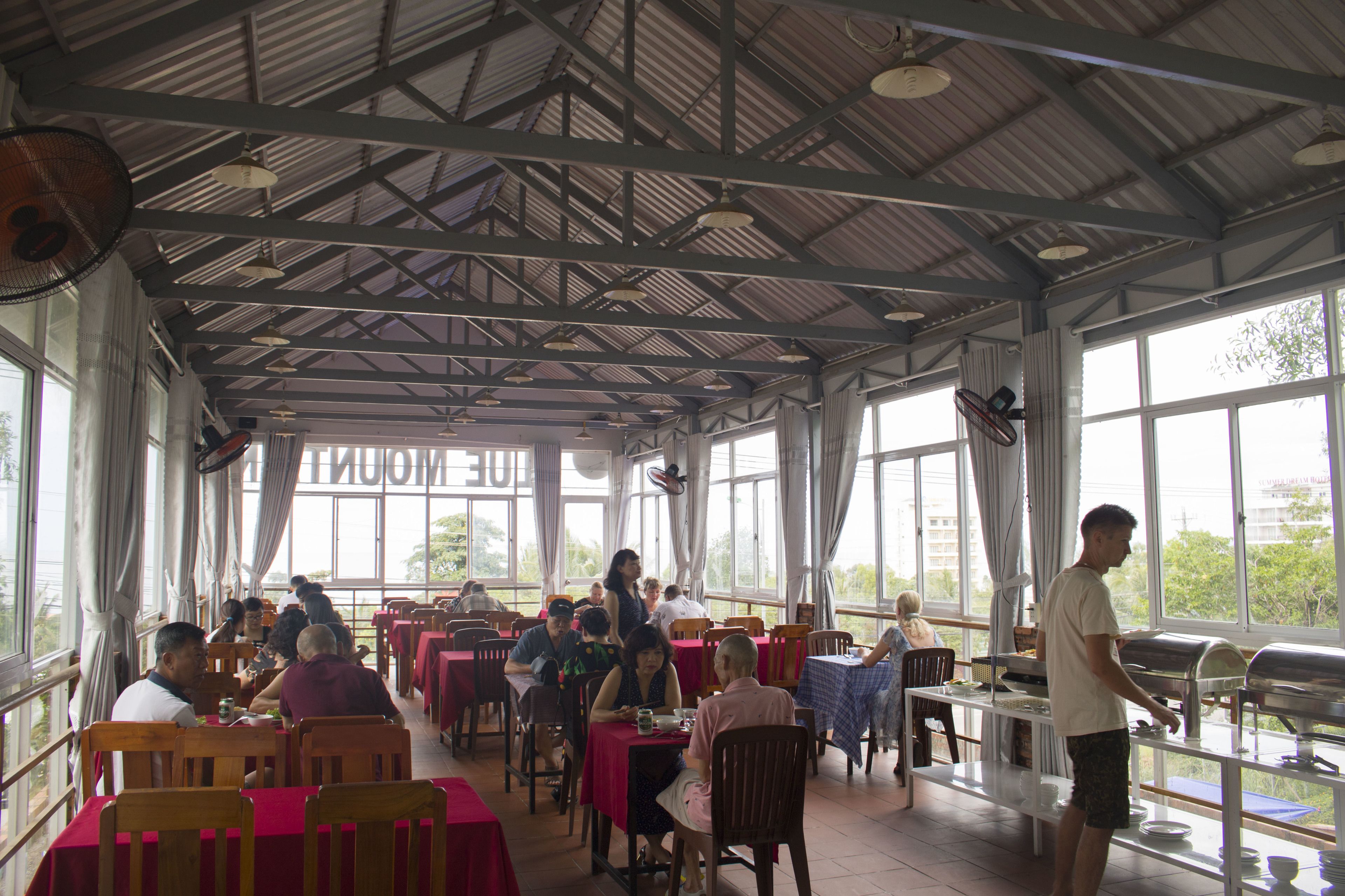 A cafeteria with tables and chairs, large windows, and a high ceiling.
