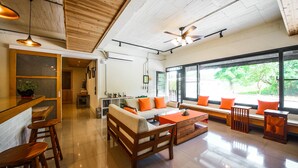 A spacious living area with a wooden ceiling, a sofa set with orange cushions, a coffee table, and a large window offering a view of greenery. - JNbnb (Beinan)
