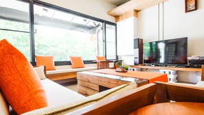A modern living room with a large window, a flat-screen TV, and a cozy seating area with orange cushions. - JNbnb (Beinan)