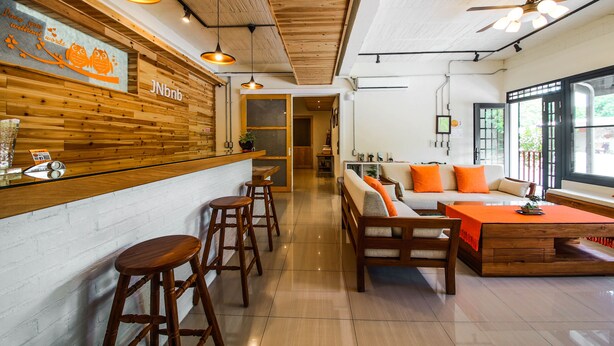 A modern interior with a wooden bar area, seating with orange cushions, and a ceiling fan. - JNbnb (Beinan)