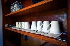 Un estante de madera con botellas de agua y tazas blancas.