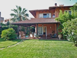 Una casa de dos pisos con un porche cubierto, un césped cuidado y diversas plantas.