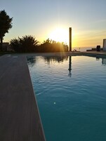 Una piscina con muelle de madera, rodeada de vegetación y vista al atardecer sobre el océano.