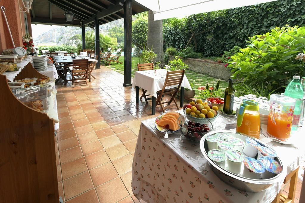 An outdoor dining area with tables and chairs, a buffet with fruits and beverages, and a garden view.