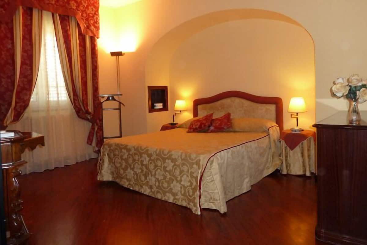Habitación de hotel con una cama grande, dos lámparas de noche, un aparador y un espejo.