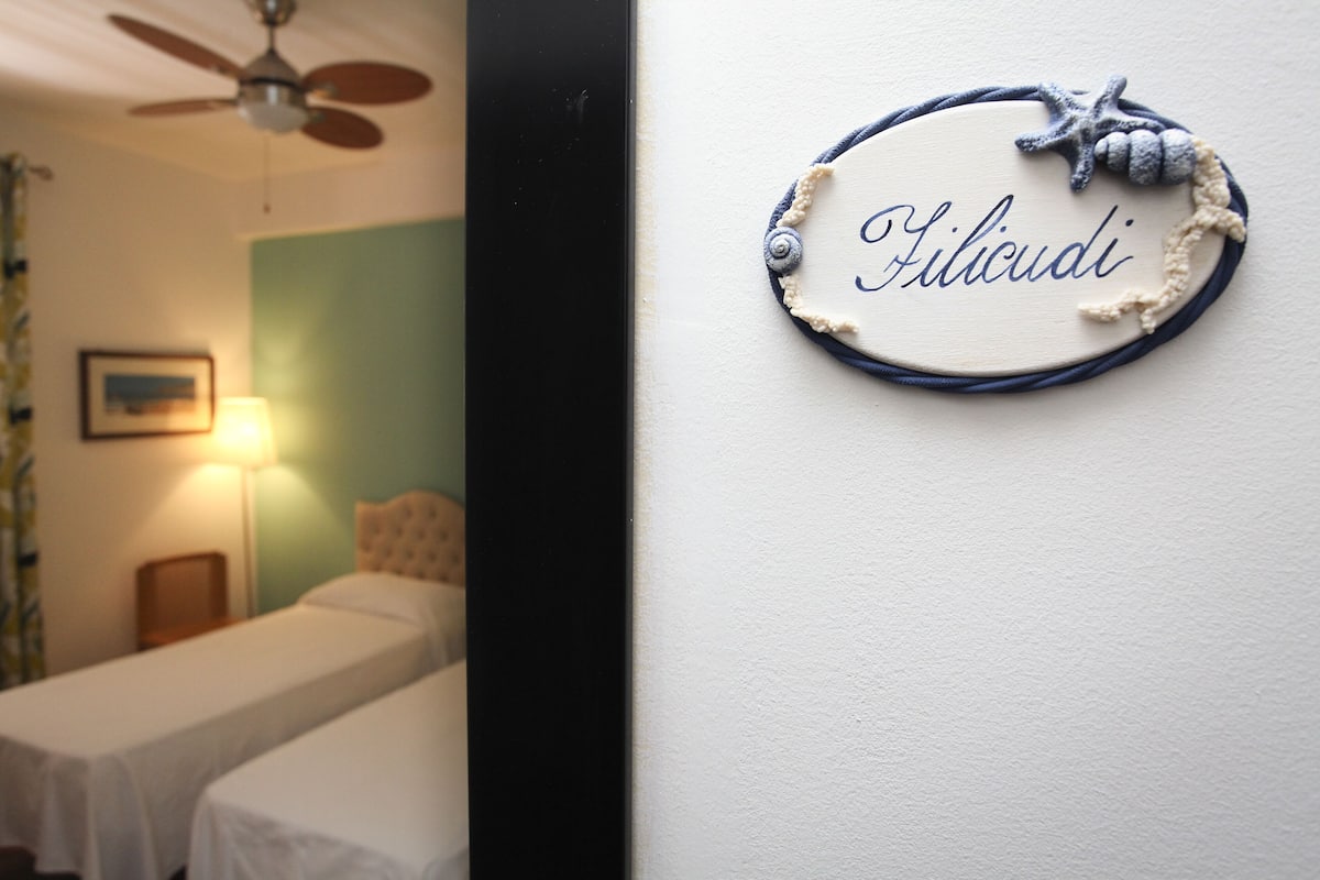 Una habitación con dos camas, un ventilador de techo, una lámpara y un letrero en la pared con el nombre 