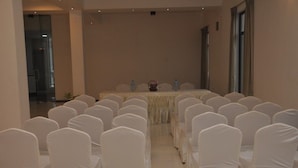 Una sala conferenze con file di sedie bianche e un tavolo con bottigliette d'acqua e un vaso di fiori.