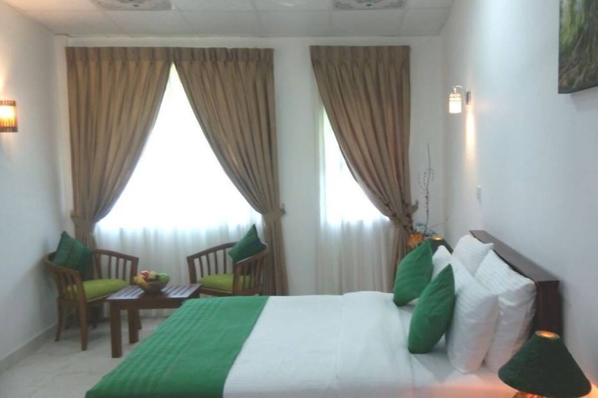 Una habitación de hotel con una cama, dos sillas, una mesita con fruteros y una lámpara.