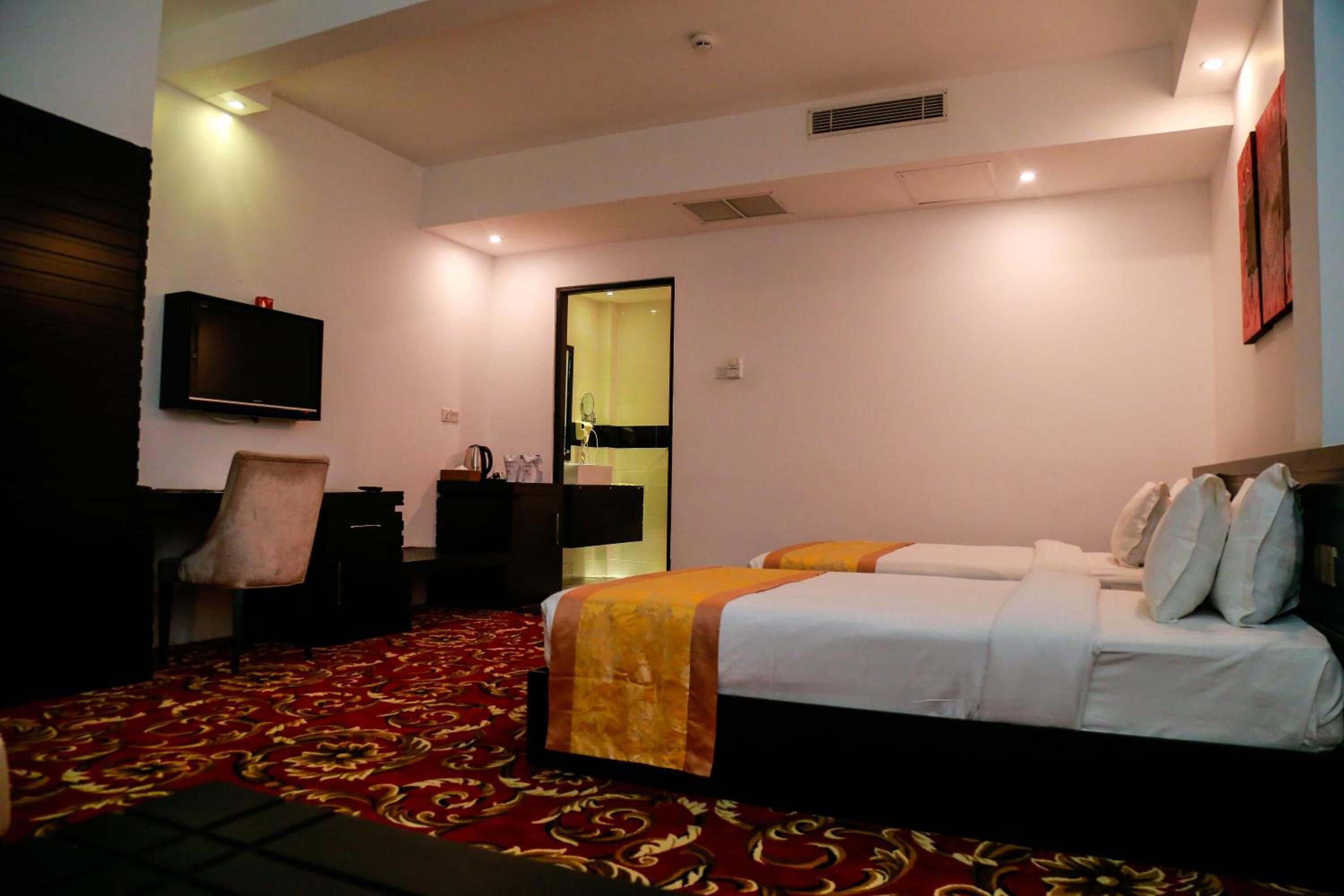 A hotel room with a bed, a desk, a chair, a television, and a bathroom visible through the door.