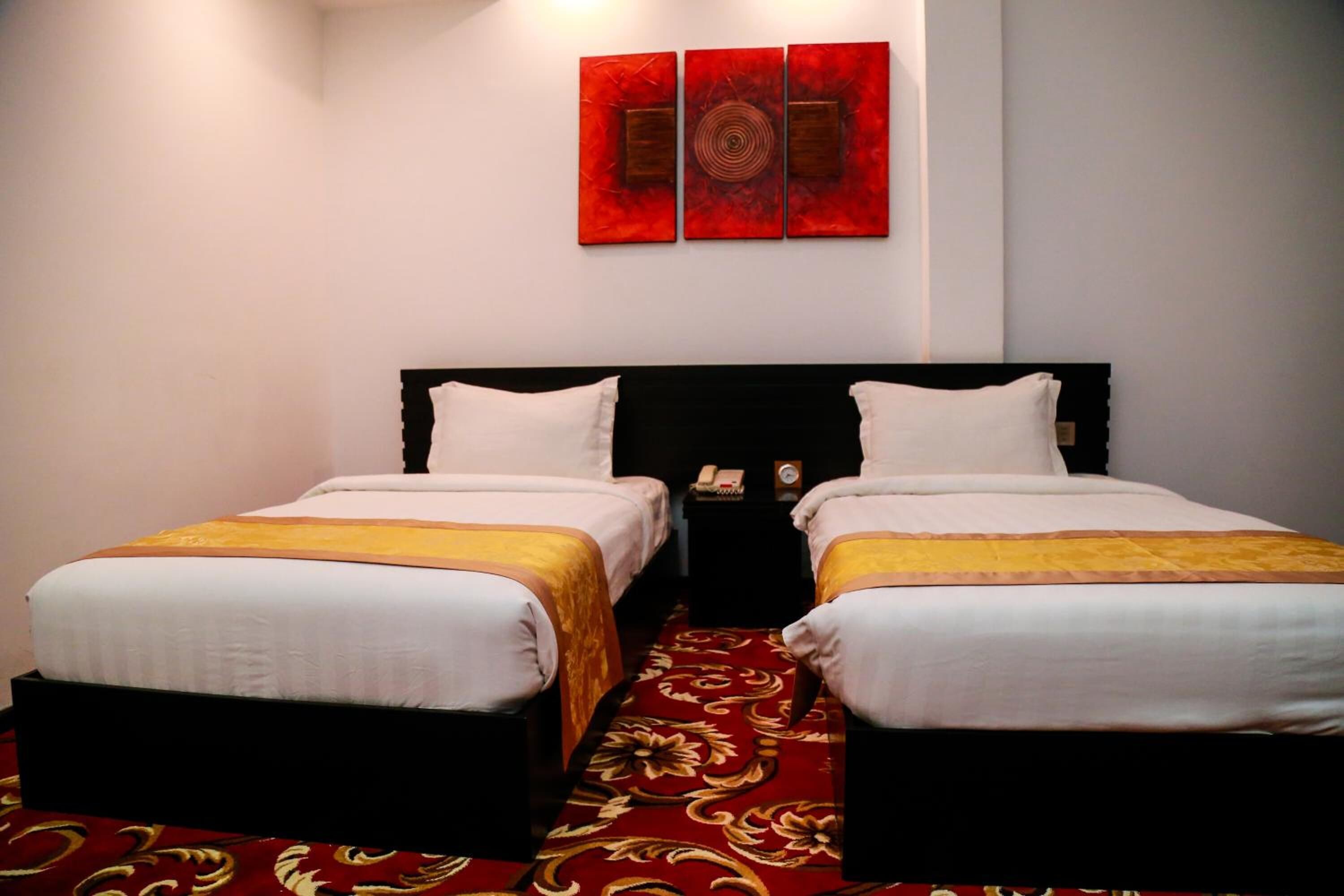 A hotel room with two single beds, a red carpet, and a wall with three red artwork pieces.