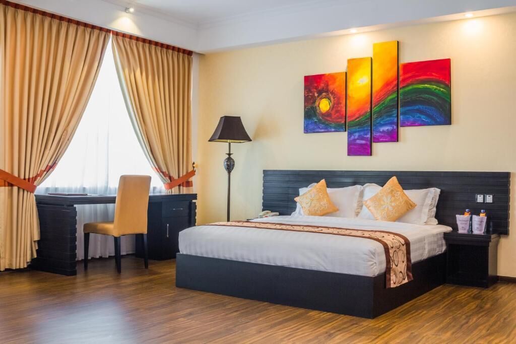 Une chambre d’hôtel avec un lit, un bureau, une chaise et un tableau au mur.