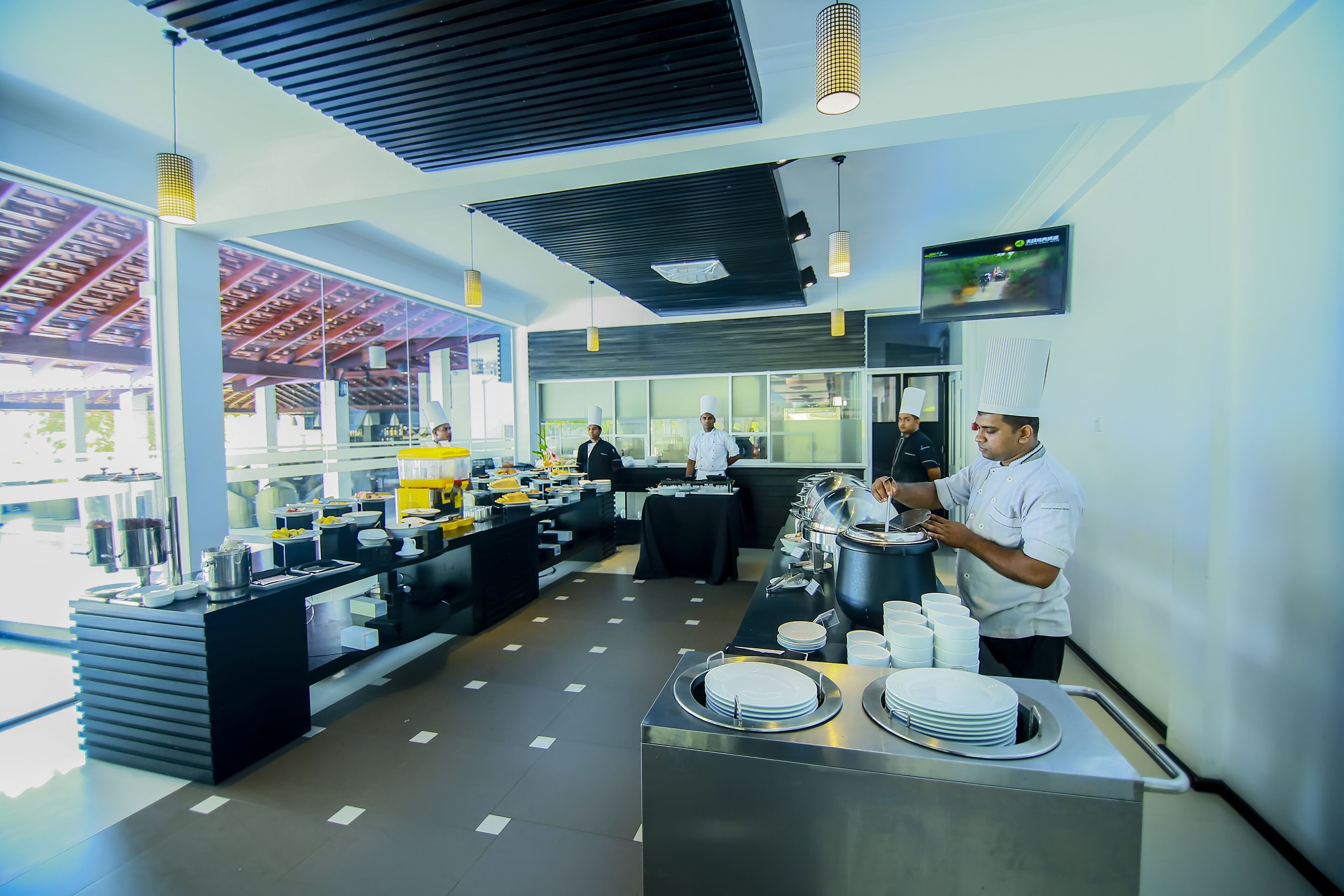 A modern kitchen with stainless steel counters, a buffet setup, and a television mounted on the wall.