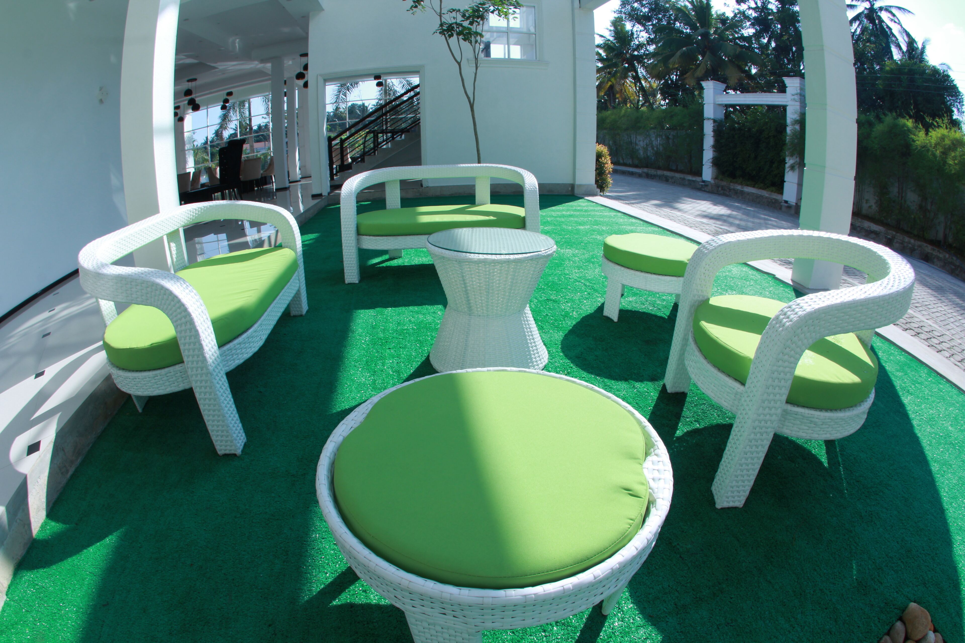 A covered outdoor seating area with white wicker furniture and green cushions.