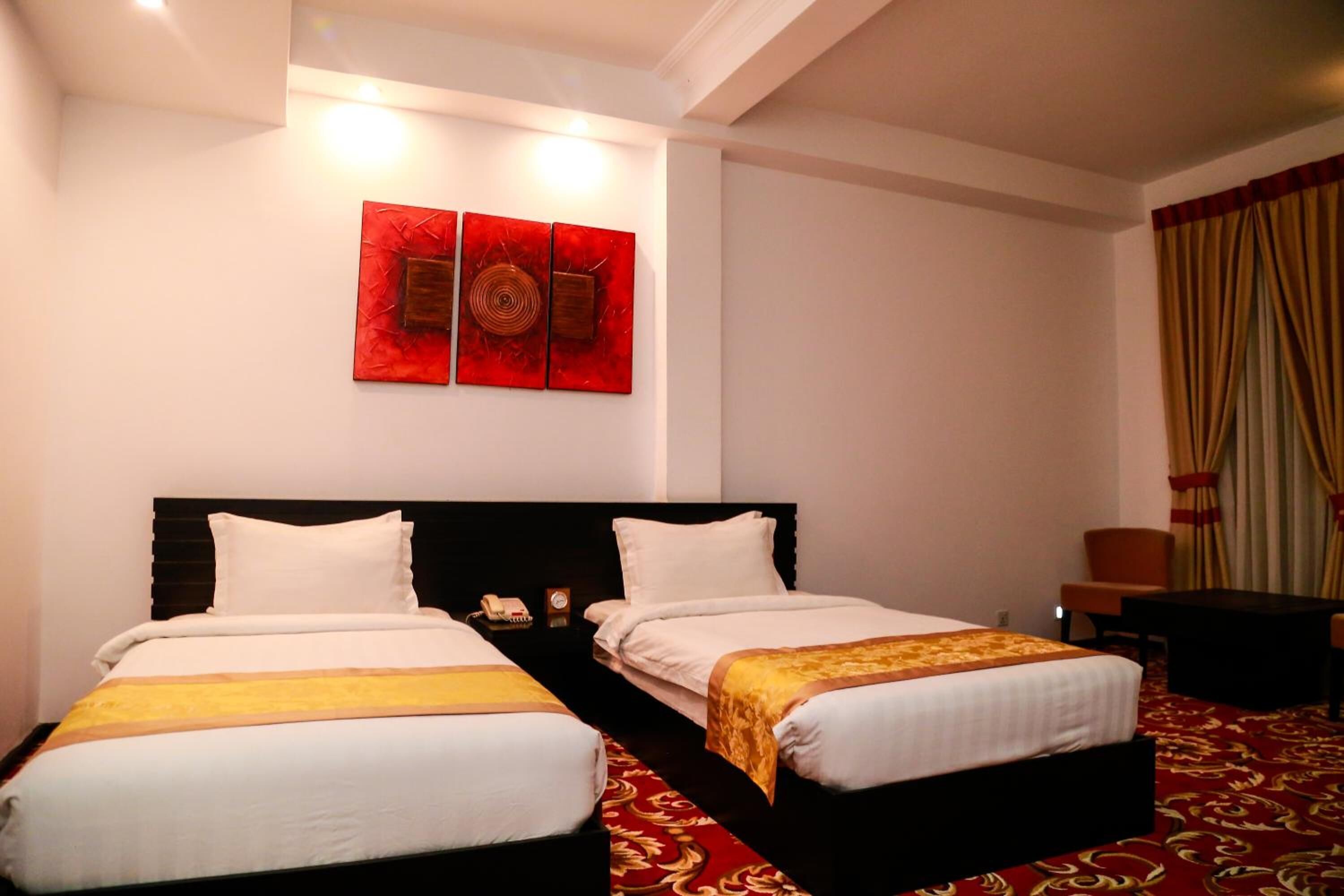 Habitación de hotel con dos camas, alfombra roja, una pared con tres obras de arte rojas y una cortina en la ventana.