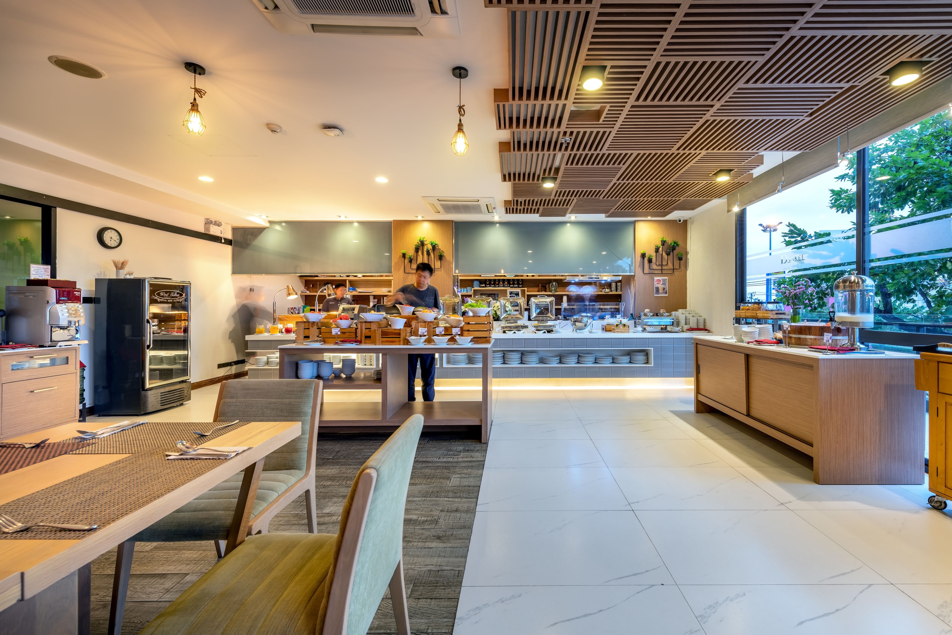 En modern restaurang med en central köksö, ett sittområde och köket synligt i bakgrunden.