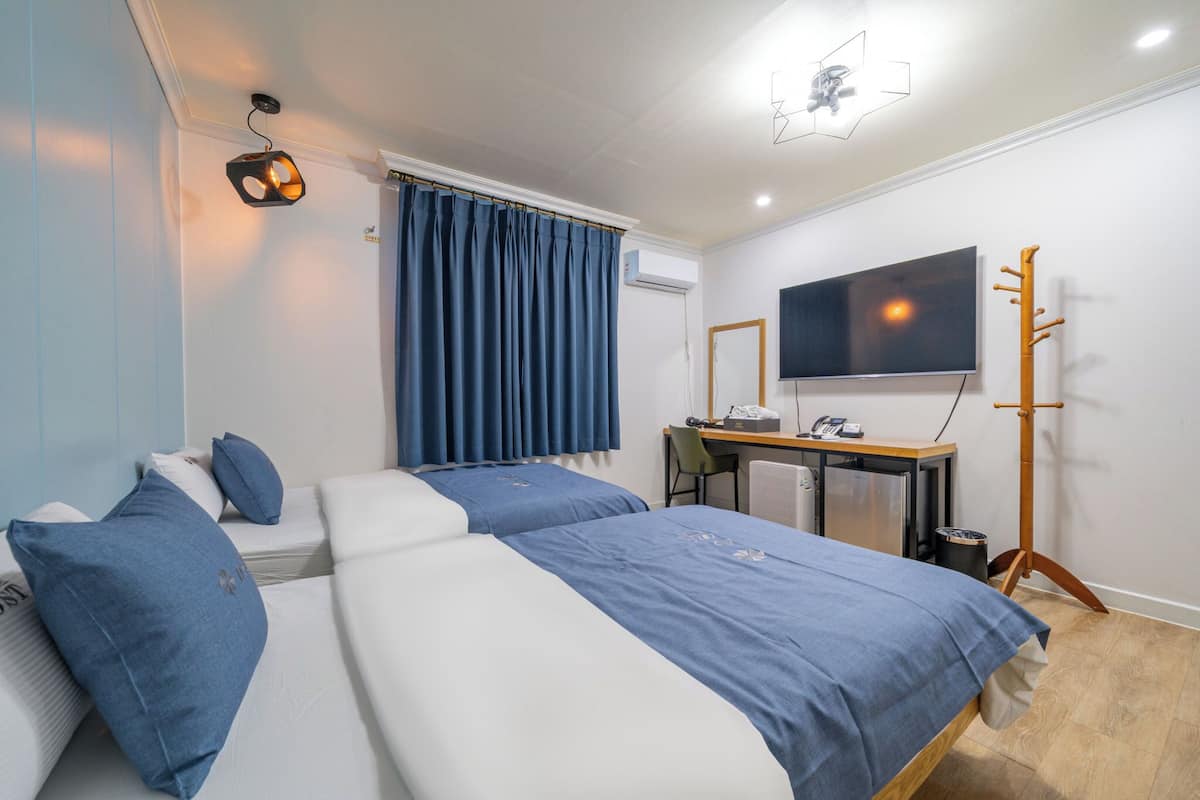 A hotel room with two beds, a desk, a chair, a television, and a wardrobe.