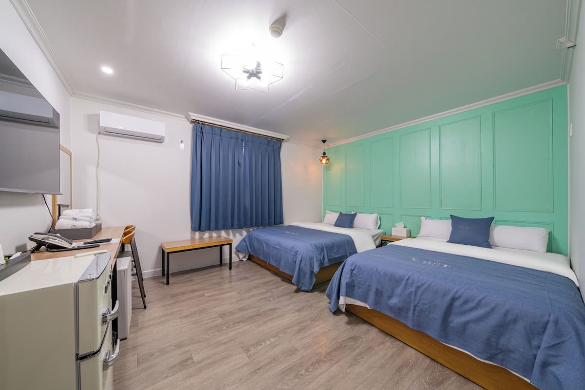 A hotel room with two beds, a desk, a chair, an air conditioning unit, and a ceiling light fixture.