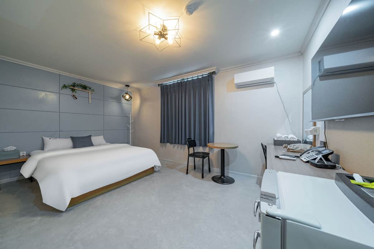 A modern hotel room with a large bed, a desk with a telephone, and a small table.