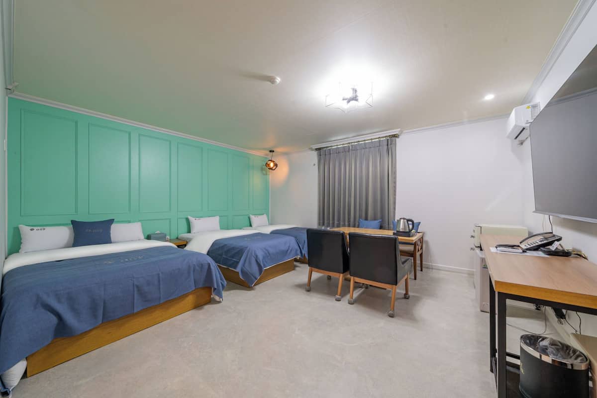 A hotel room with two beds, a desk, a chair, a small table, a telephone, and an air conditioning unit.