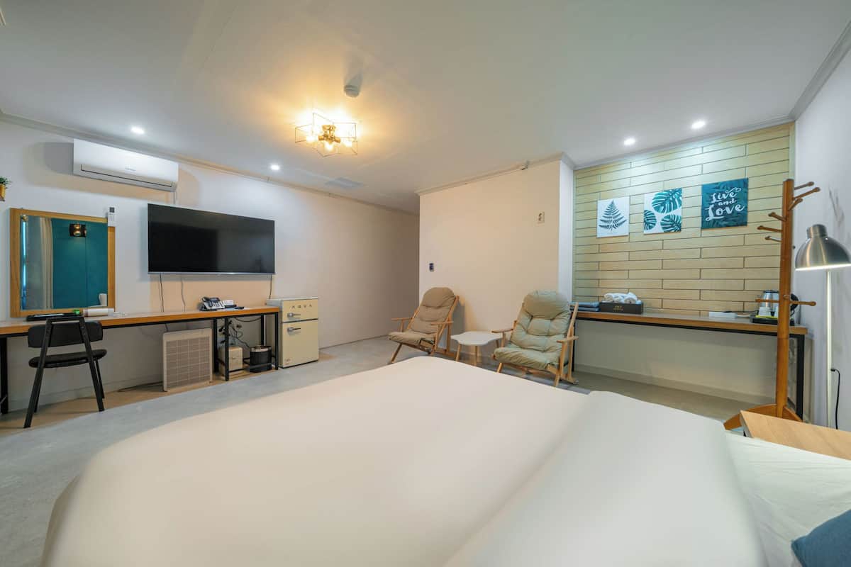 A hotel room with a bed, desk, chairs, a TV, and artwork on the wall.