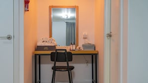 A small, narrow room with a wooden desk, a black chair, a mirror, and a small table with toiletries. - OST Hotel (Chuncheon)