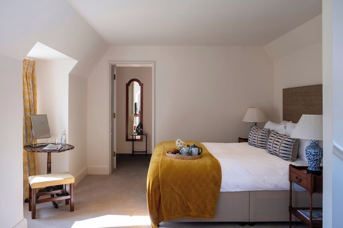 A bedroom with a bed, bedside tables, a desk with a chair, a mirror, and a window with curtains.