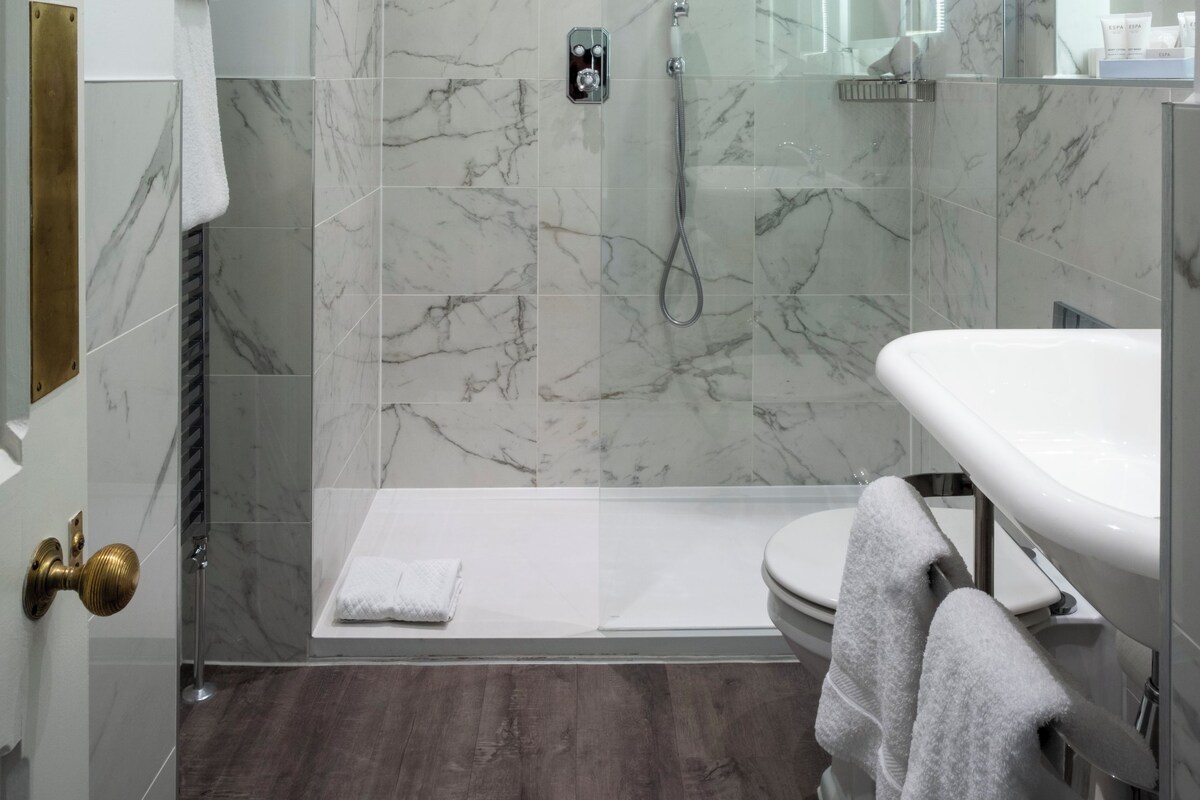 Un baño moderno con ducha de vidrio, un lavamanos blanco y pared de ducha con azulejos de mármol.