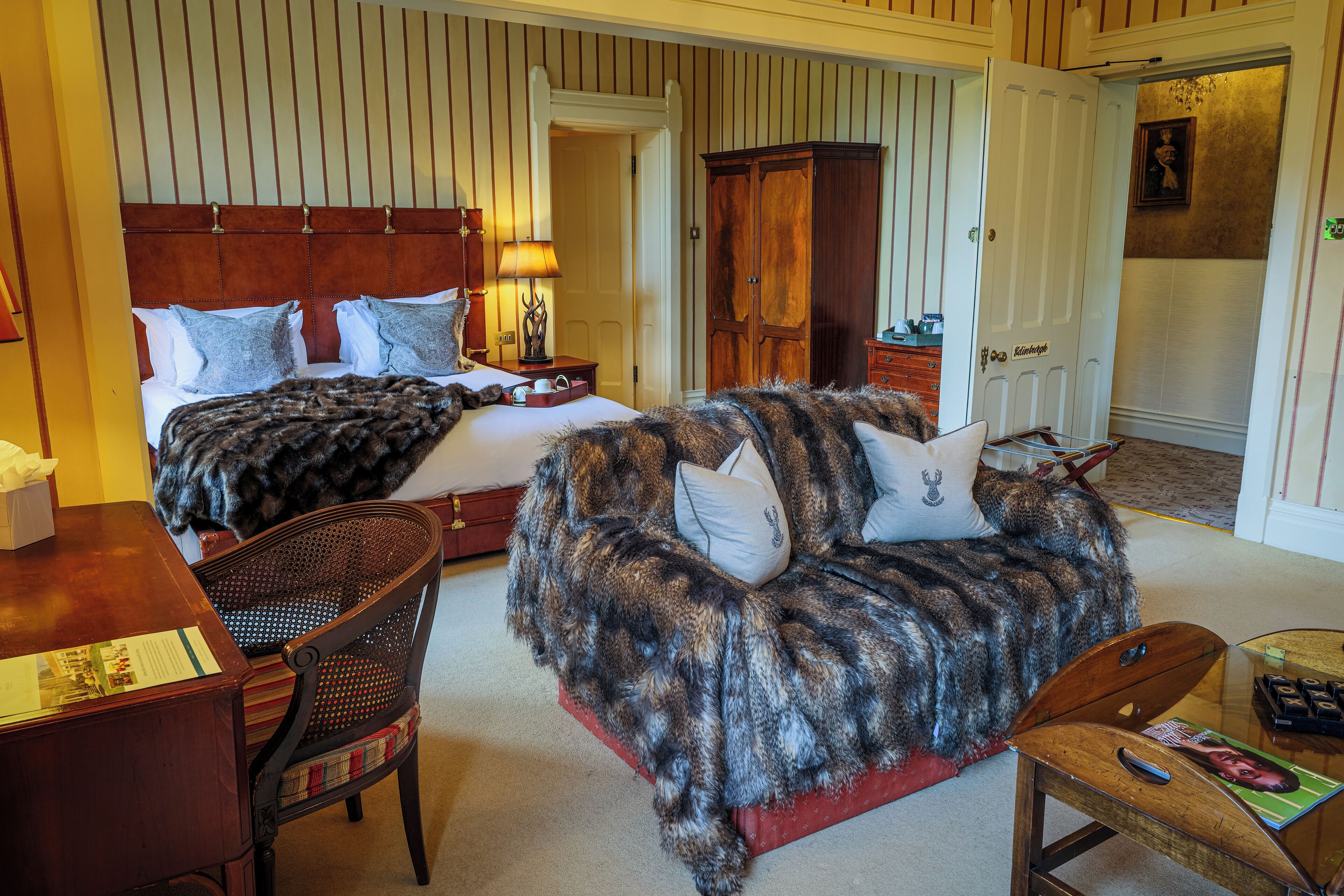 A hotel room with two beds, a fur-covered sofa, a wooden desk, and a chair.