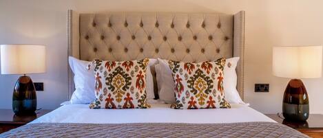 A neatly made bed with a quilted cover, a tufted headboard, and two matching lamps on either side.