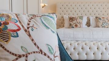 Un dormitorio con cabecera capitonada, almohadas estampadas con motivos florales y una cama con edredón blanco.