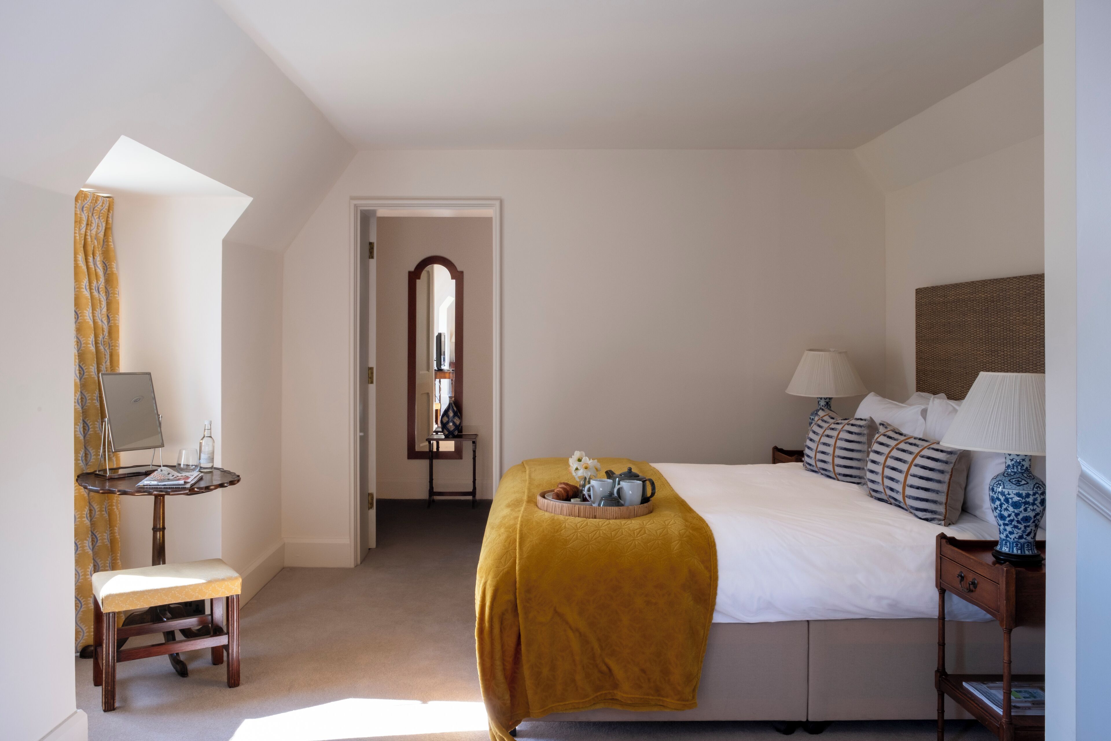 A bedroom with a bed, bedside tables, a desk with a chair, a mirror, and a window with curtains.