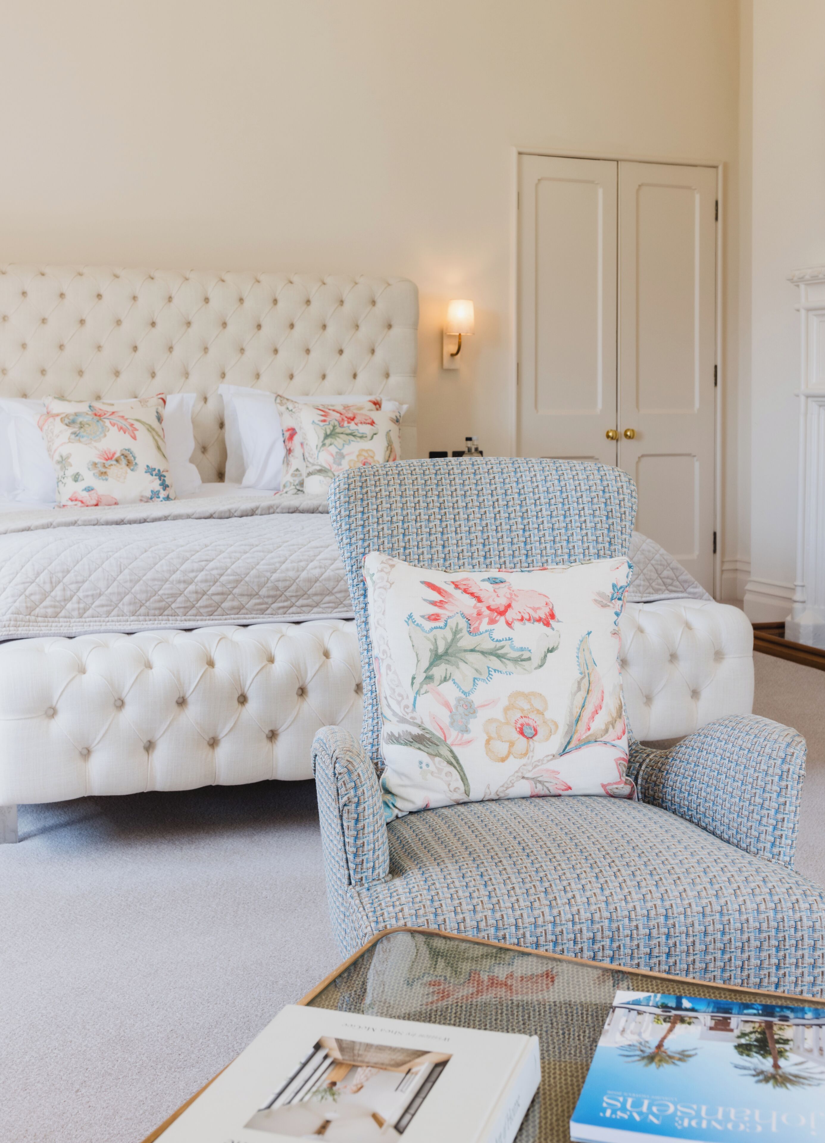 Ein Schlafzimmer mit einem karottenartig gepolsterten Kopfteil, einem armchair mit Blumenmuster und einem Nachttisch mit einem Buch.