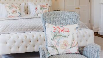 Ein Schlafzimmer mit einem karottenartig gepolsterten Kopfteil, einem armchair mit Blumenmuster und einem Nachttisch mit einem Buch.