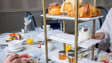A breakfast setting with a three-tiered stand holding pastries, a glass of orange juice, and condiments on a marble table.