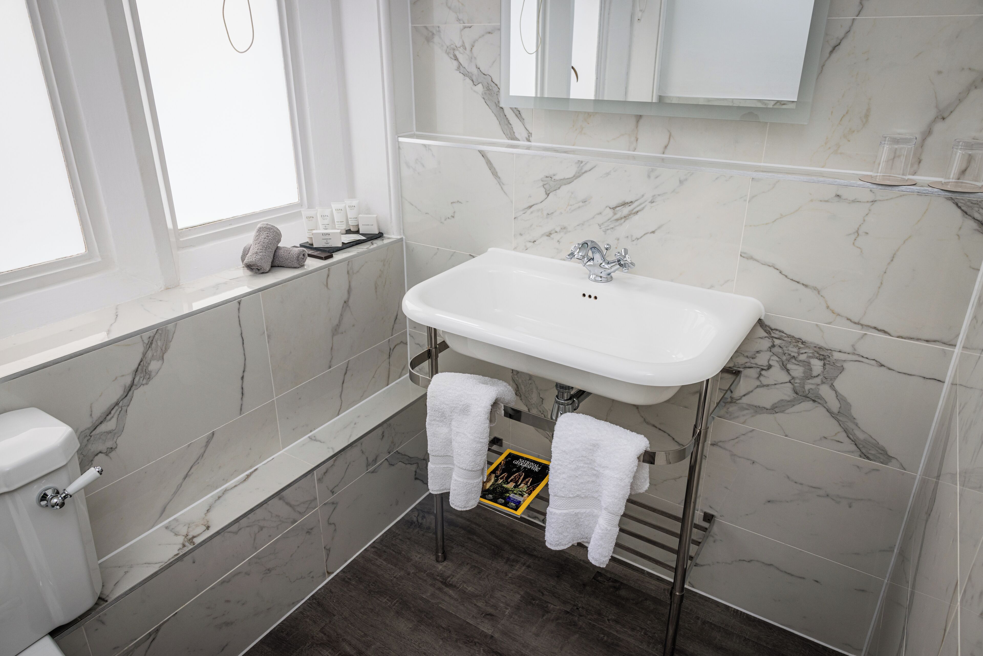 A bathroom with a white sink, marble walls, and a bathtub.