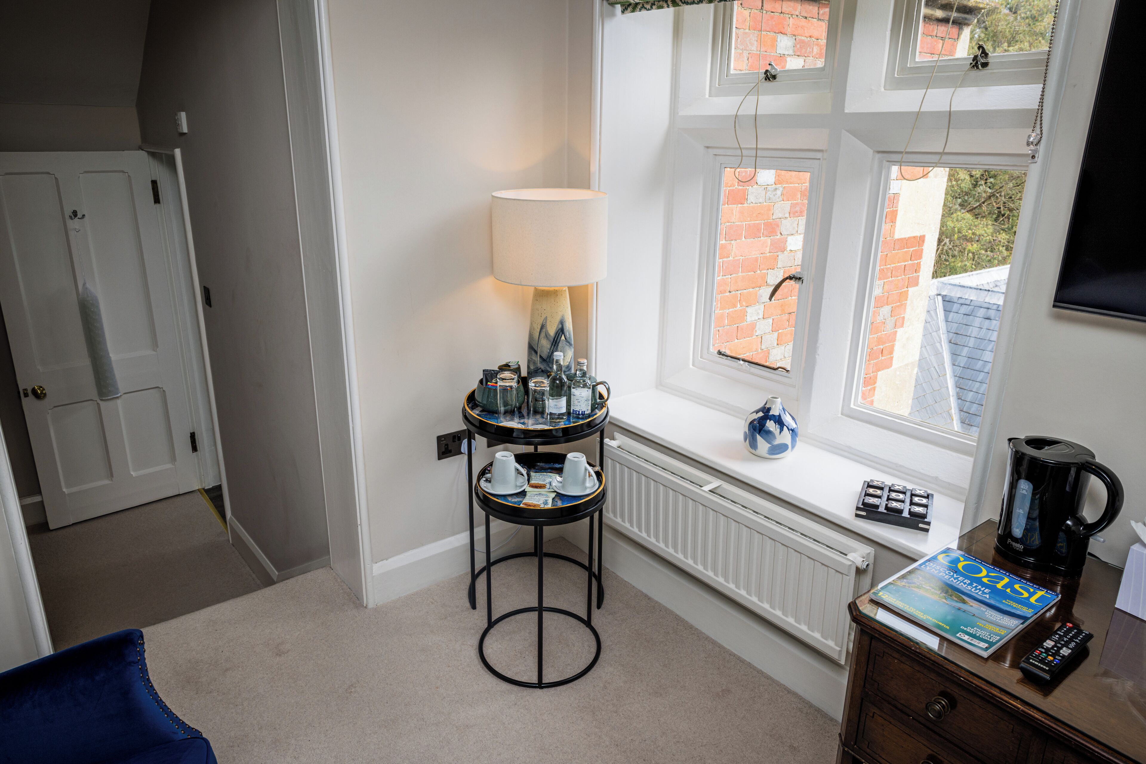 Een gezellige kamer met een raam, een tafel met een lamp, een radiator en een boekenkast.