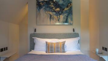 A modern hotel room with a large bed, a painting above it, and two armchairs.