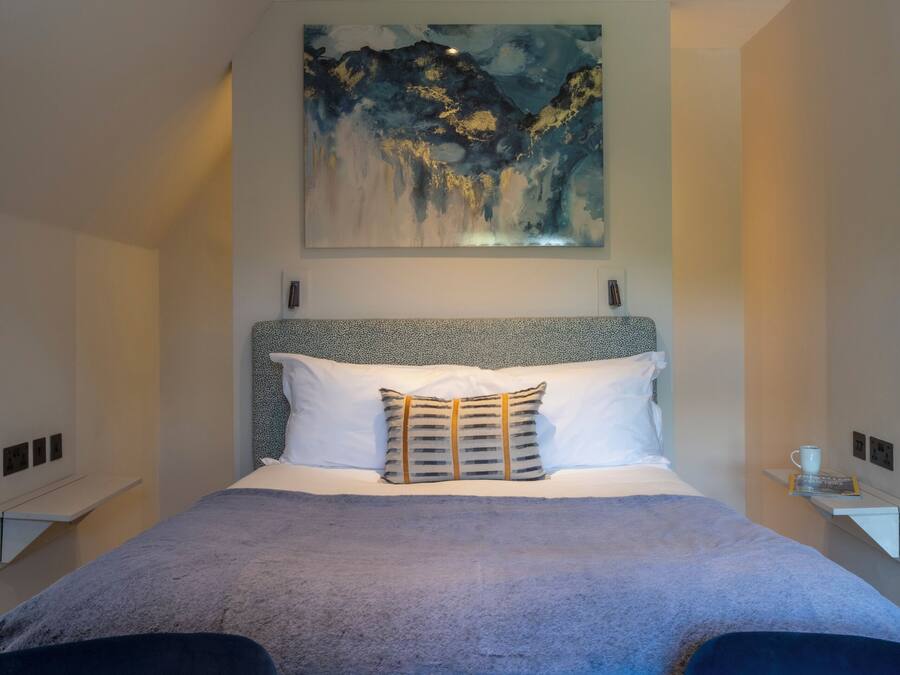A modern hotel room with a large bed, a painting above it, and two armchairs.
