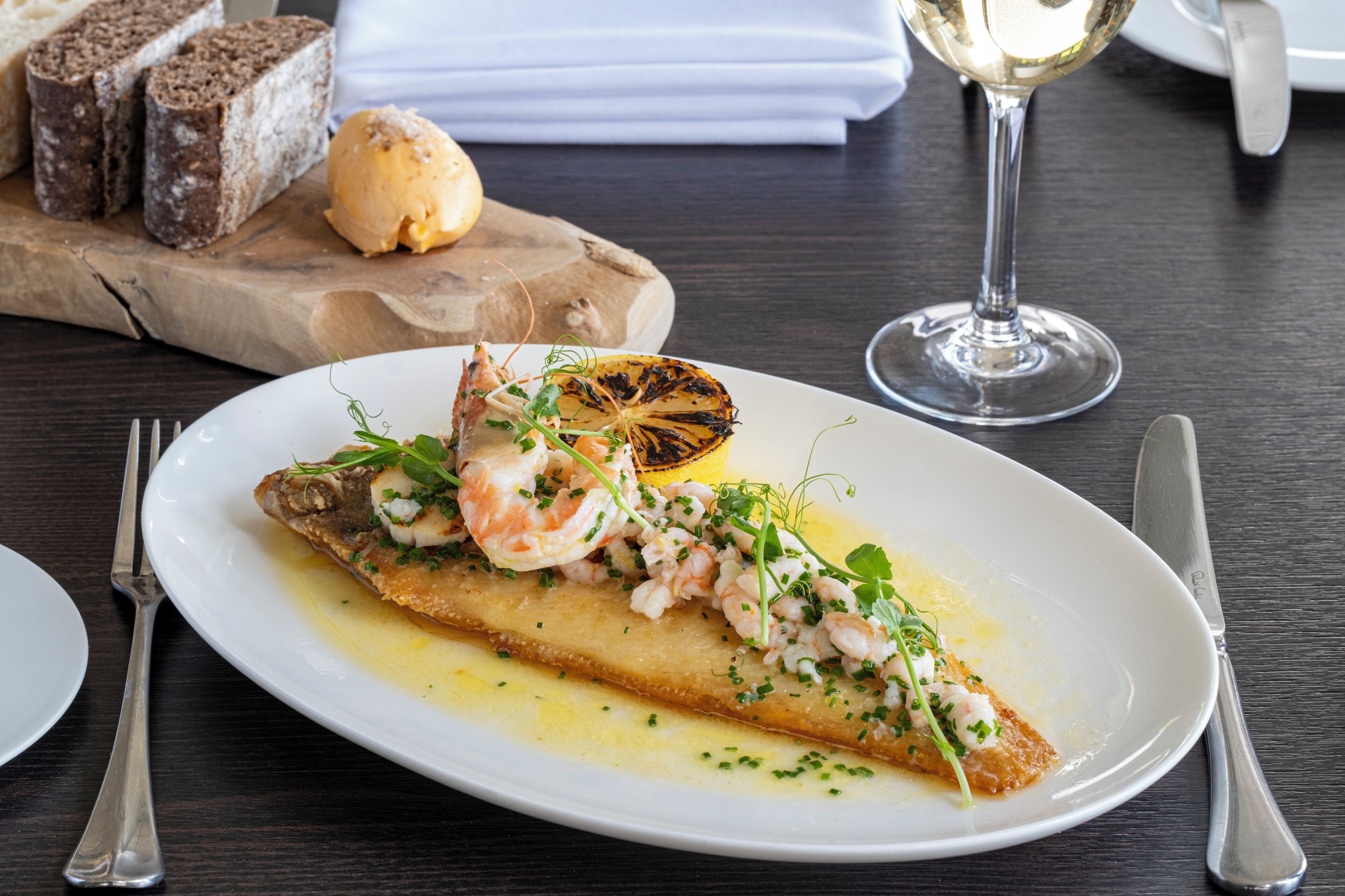 Un plato de comida con camarones, hierbas y una rodaja de limón sobre un plato blanco.