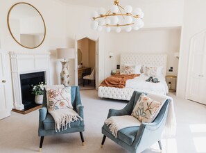 A bedroom with a fireplace, two armchairs, a bed with a headboard, and a chandelier. - Horsted Place (Uckfield)