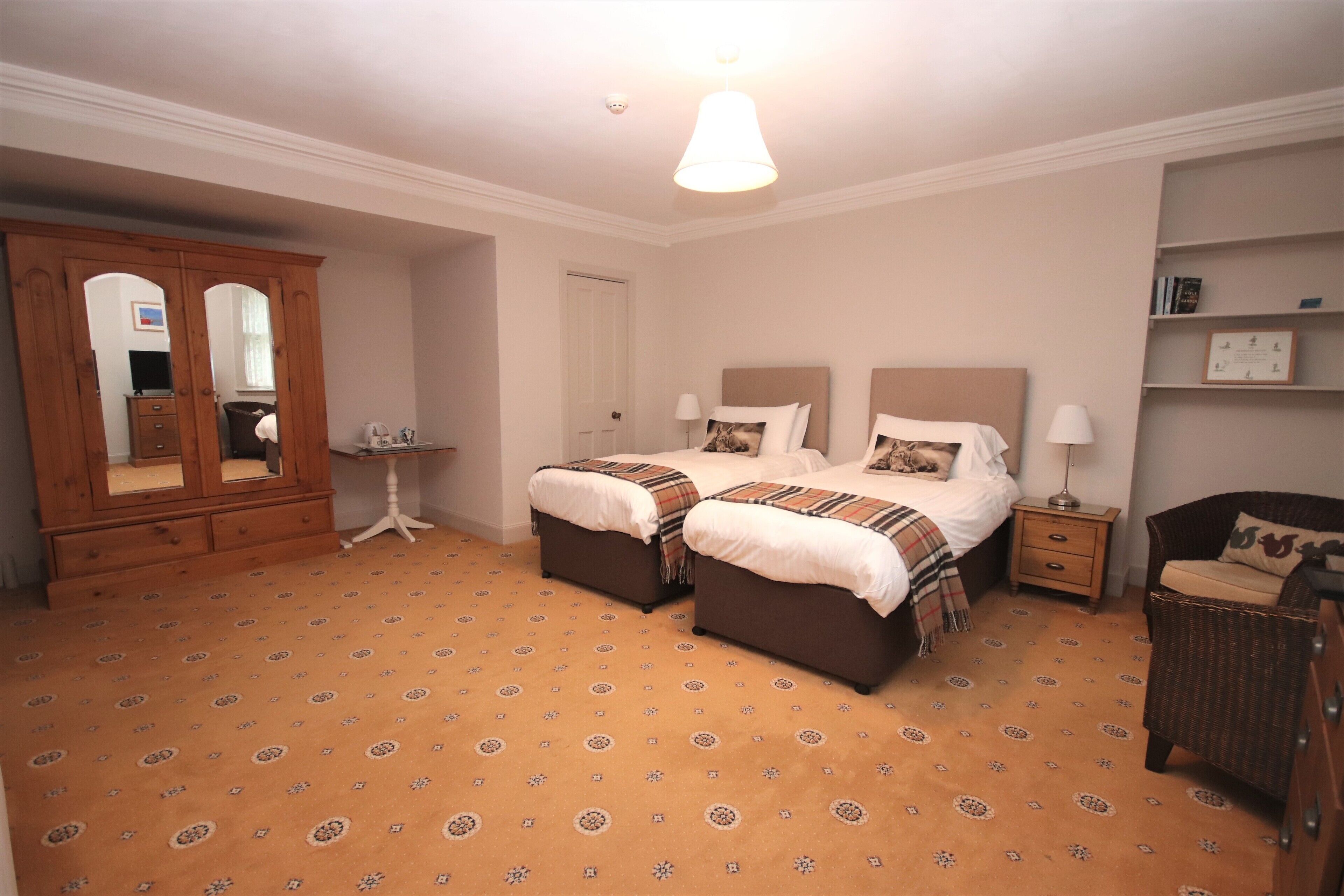 A bedroom with two beds, a wardrobe, a bedside table, a chair, and a lamp.