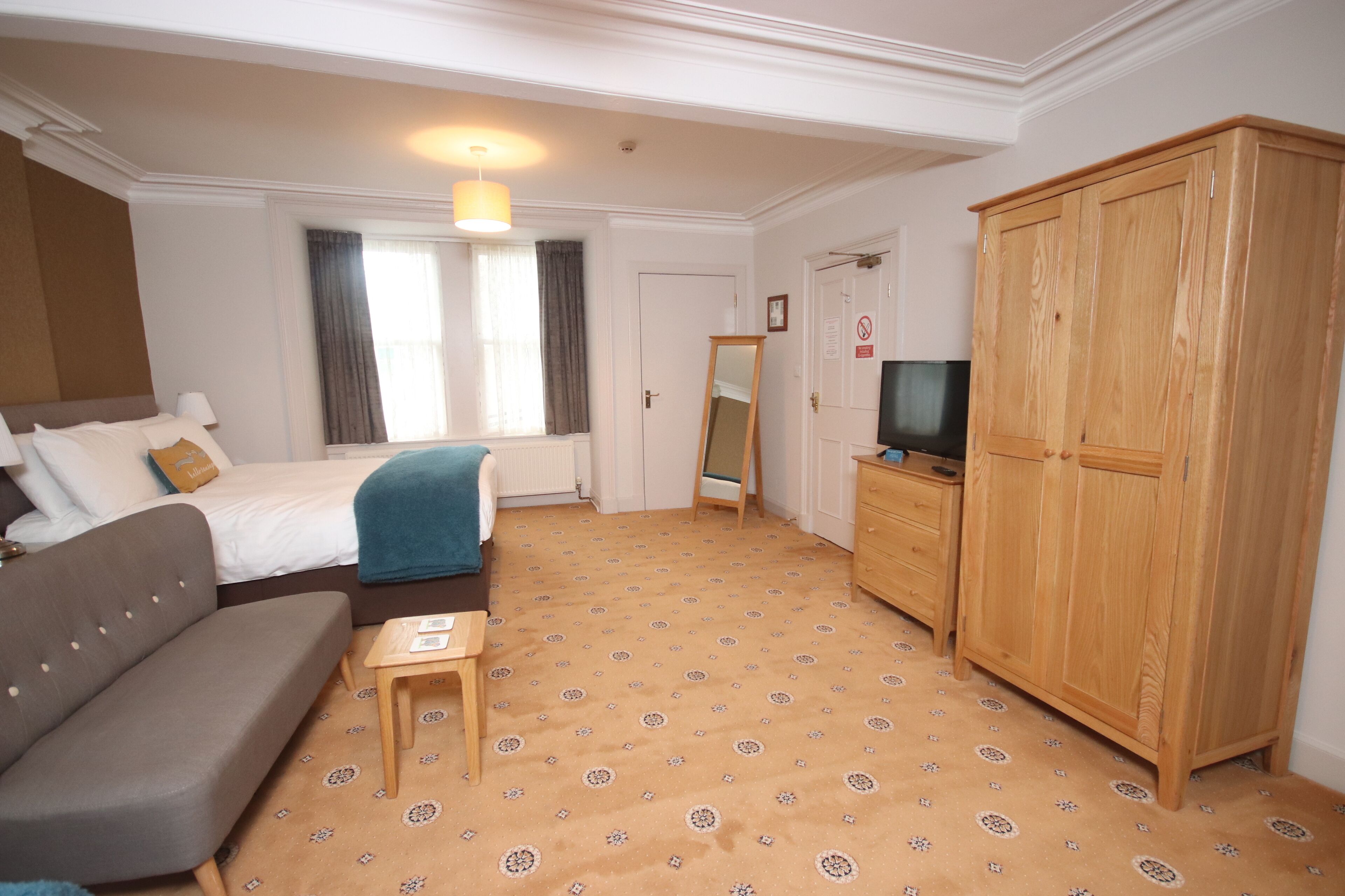 A hotel room with a bed, a sofa, a TV, a wardrobe, and a small table.