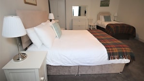 A bedroom with a large bed, a bedside table with a lamp, a dresser, a chair, and a mirror. - Inglestone House (Kelso)